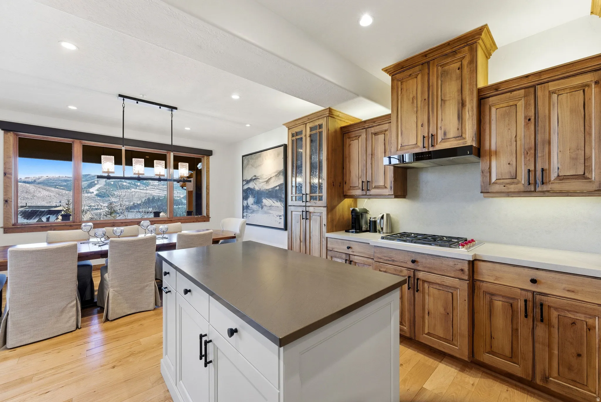 Open-concept kitchen and dining area featuring a gas cooktop, wood-finish cabinetry, a central island with a contrasting countertop, and light wood-finish flooring