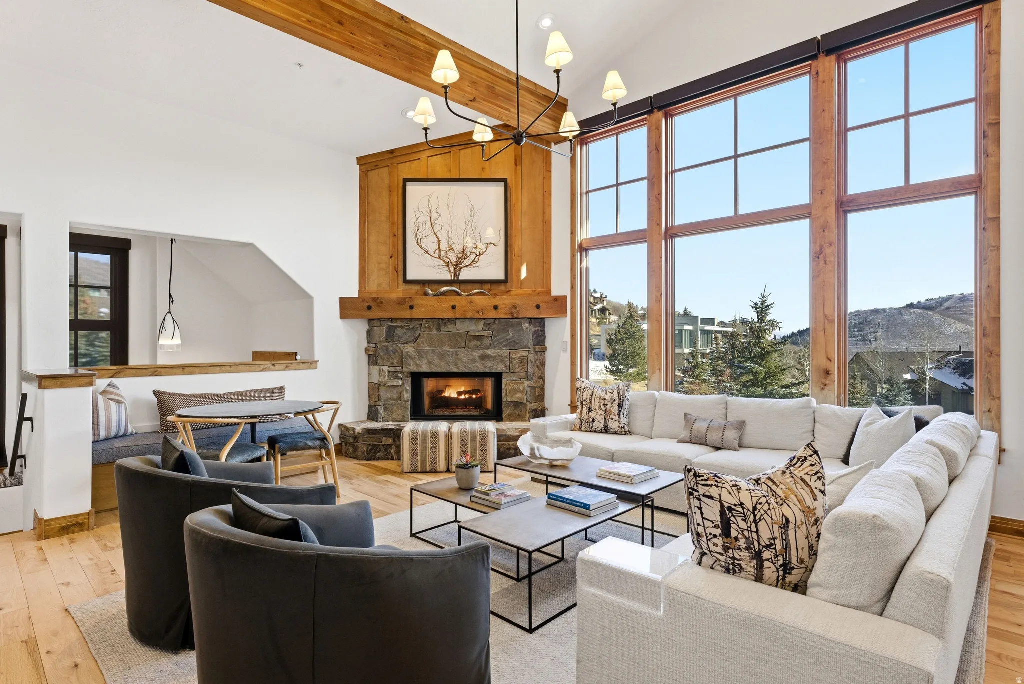 Spacious living area featuring a stone fireplace with a wood mantel, high vaulted ceilings with exposed wood beams, and a large wall of windows