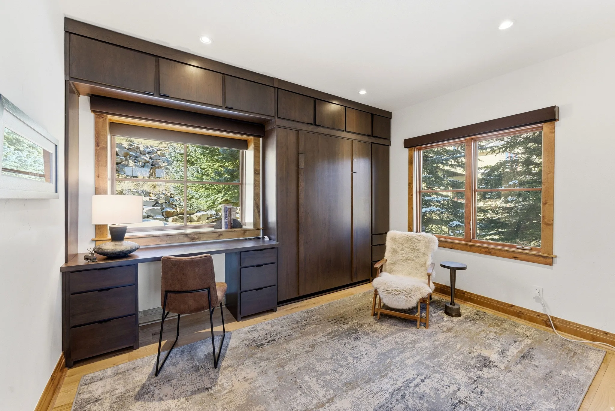 Built-in wood-finish desk with integrated drawers, wood-finish wall bed cabinetry, recessed lighting, wood-trimmed windows, and wood-finish flooring