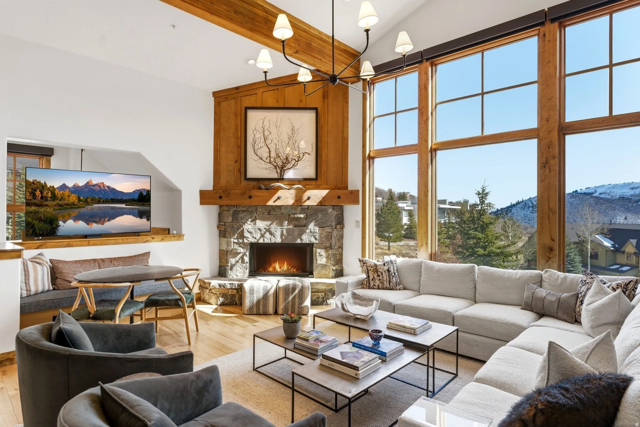 Spacious living area featuring a stone fireplace with a wood mantel, a built-in banquette, expansive multi-pane windows, and wood-finish flooring