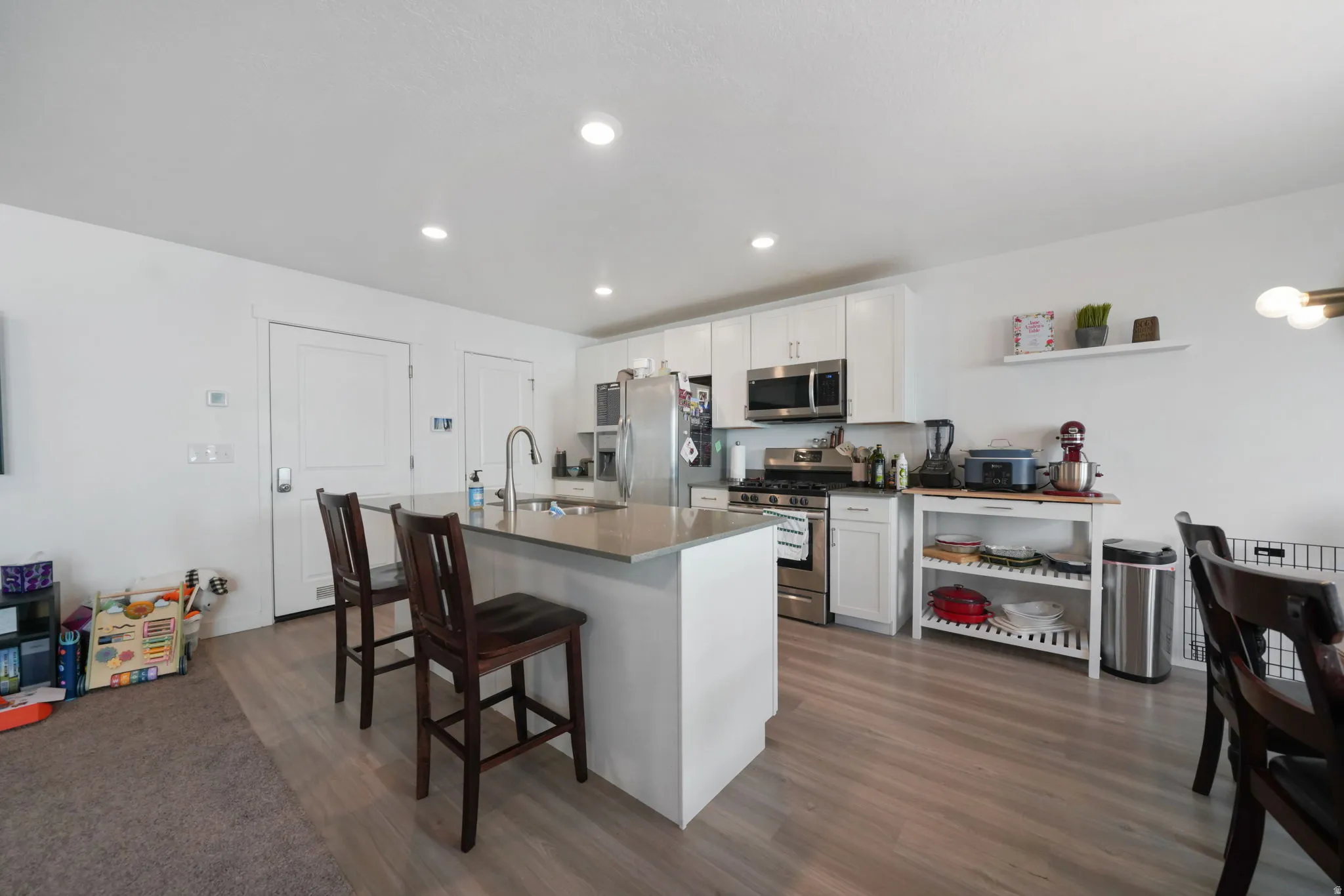 Kitchen with a kitchen bar, white cabinets, dark wood-style flooring, stainless steel appliances, and recessed lighting
