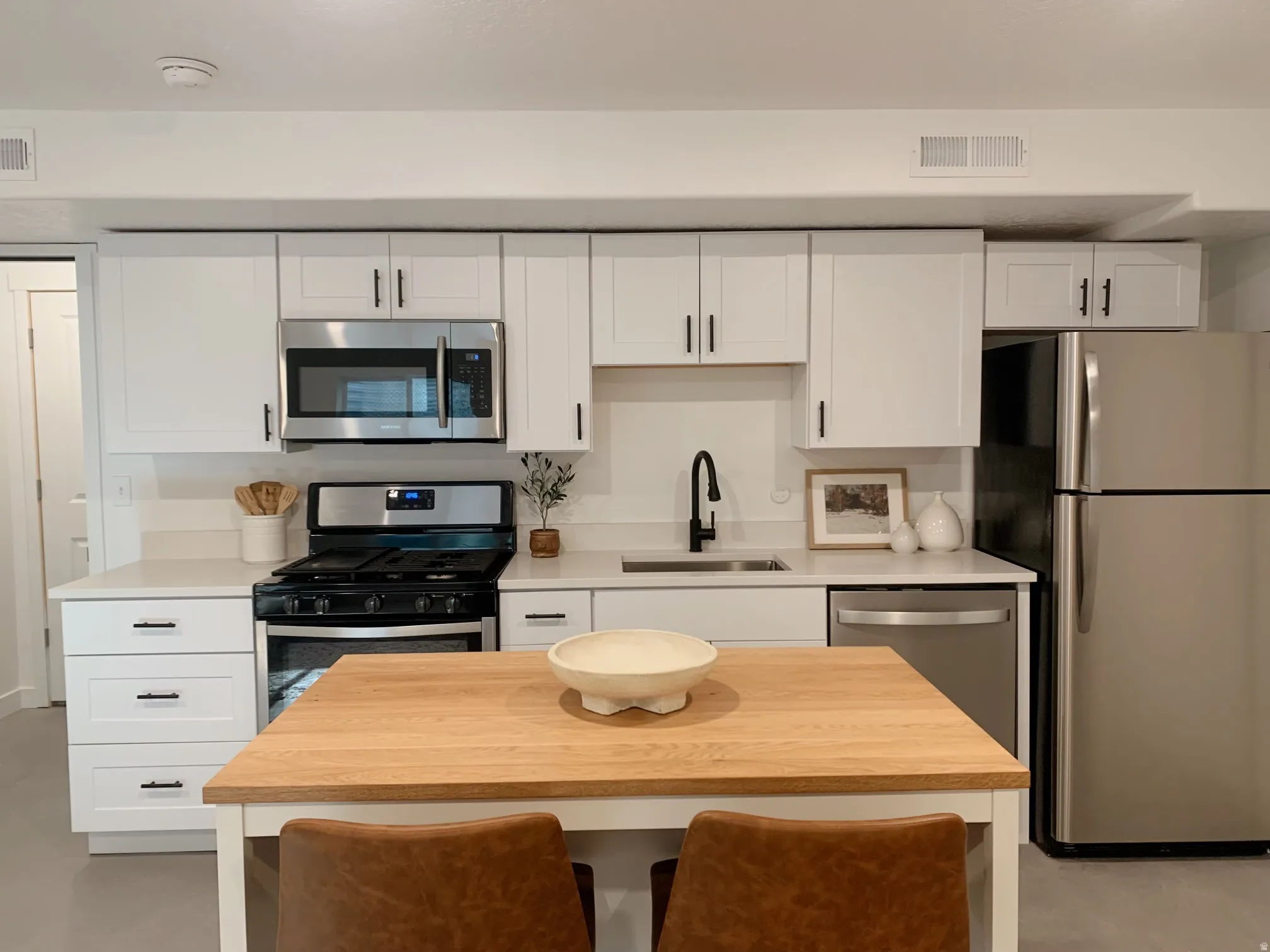 Kitchen with stainless steel appliances, white cabinetry, concrete flooring, and wood counters