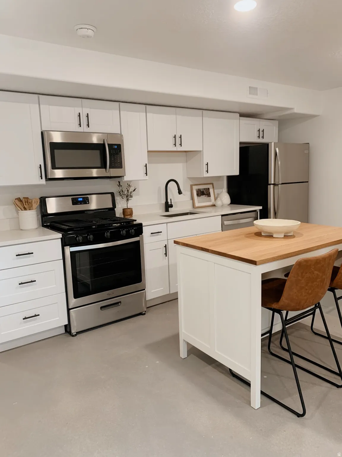 Kitchen featuring stainless steel appliances, a kitchen breakfast bar, white cabinetry, and finished concrete floors