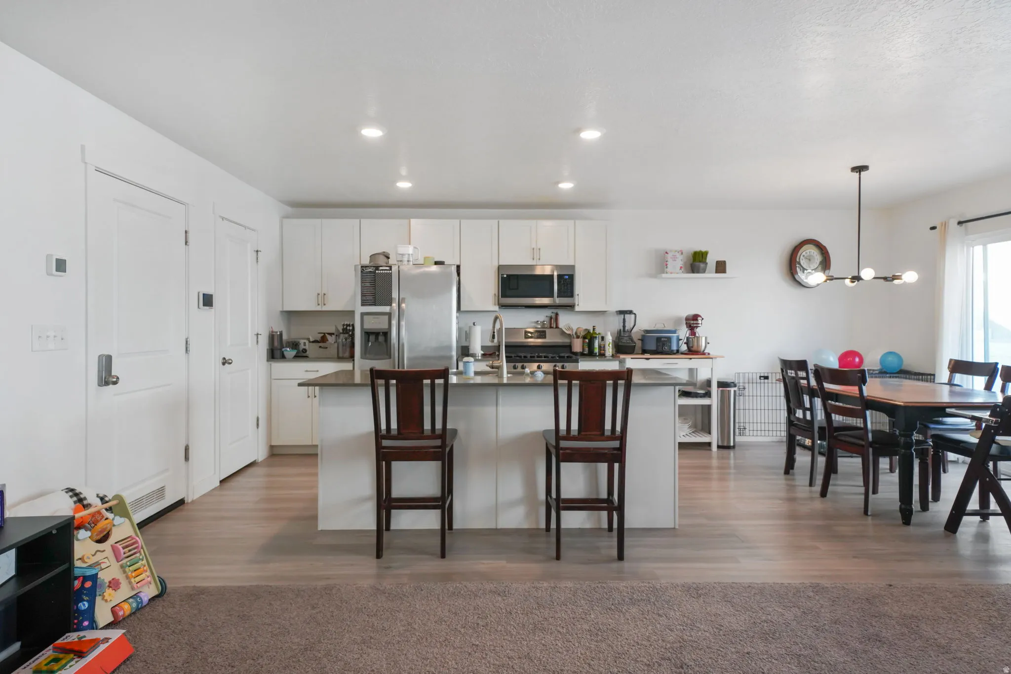 Kitchen featuring white cabinetry, stainless steel appliances, an island with sink, a kitchen bar, and dark countertops