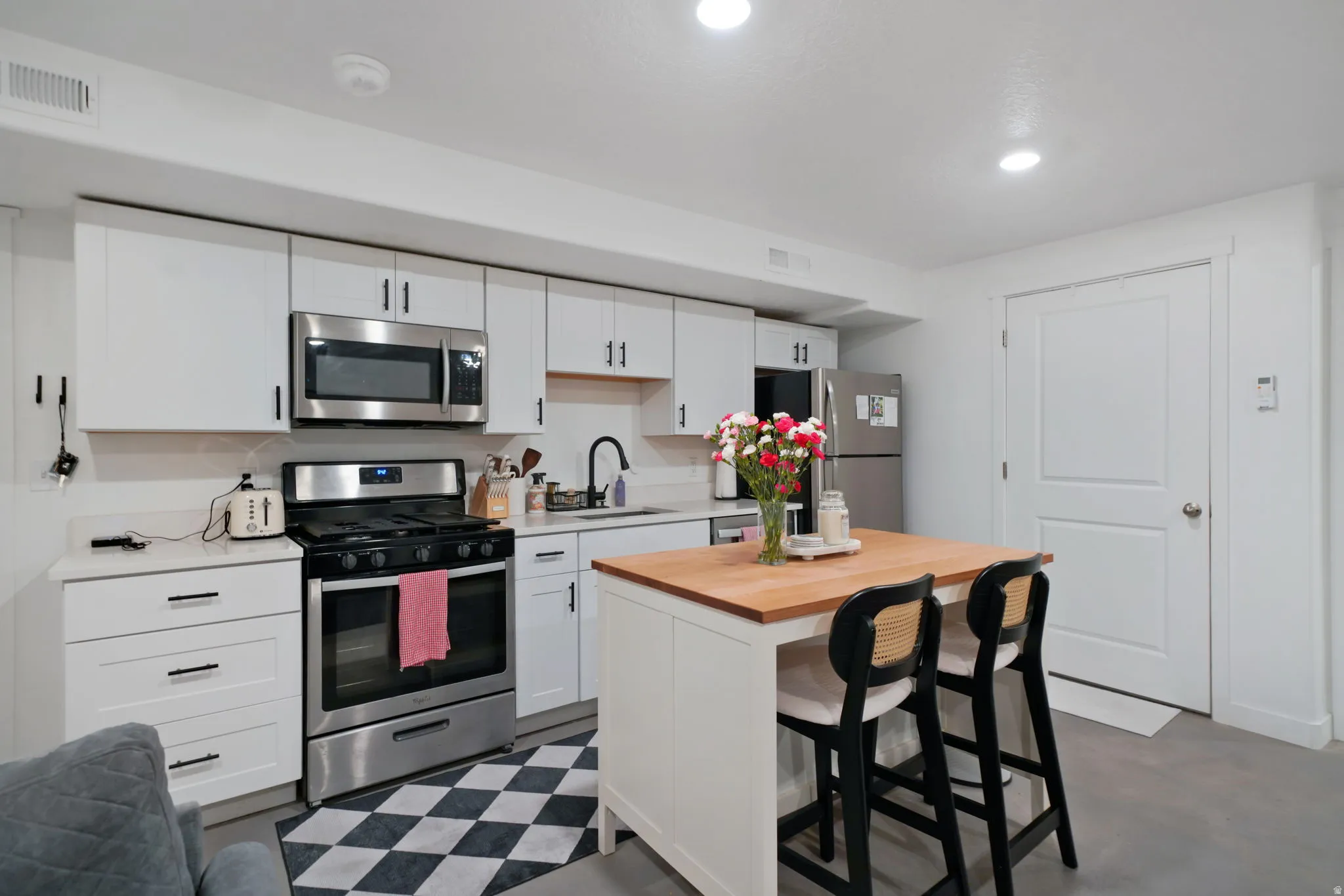 Kitchen featuring stainless steel appliances, white cabinets, a breakfast bar area, wood counters, and recessed lighting