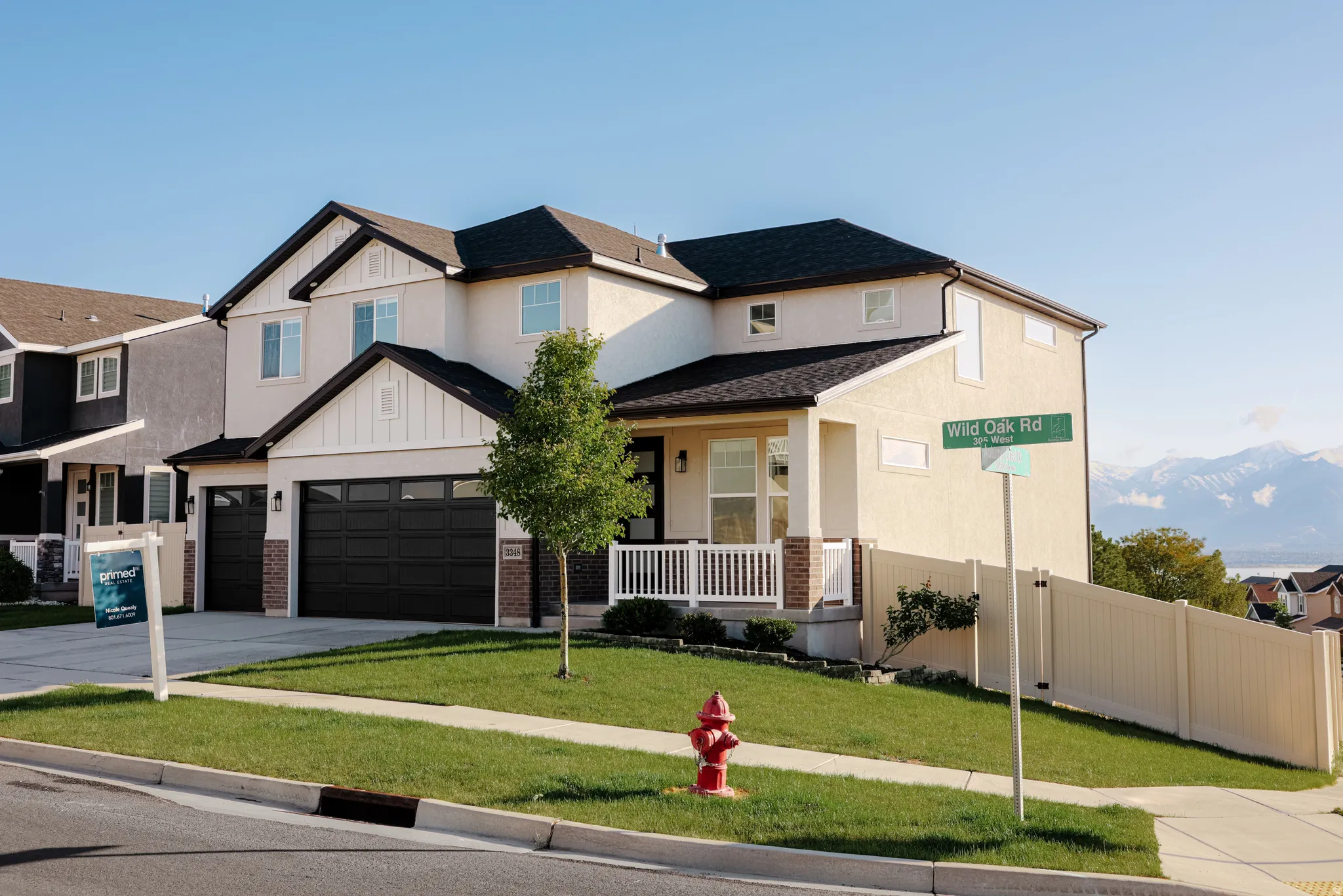 Two-story stucco and siding residence featuring a covered front porch with white railing, a two-car garage, and a sloped front lawn