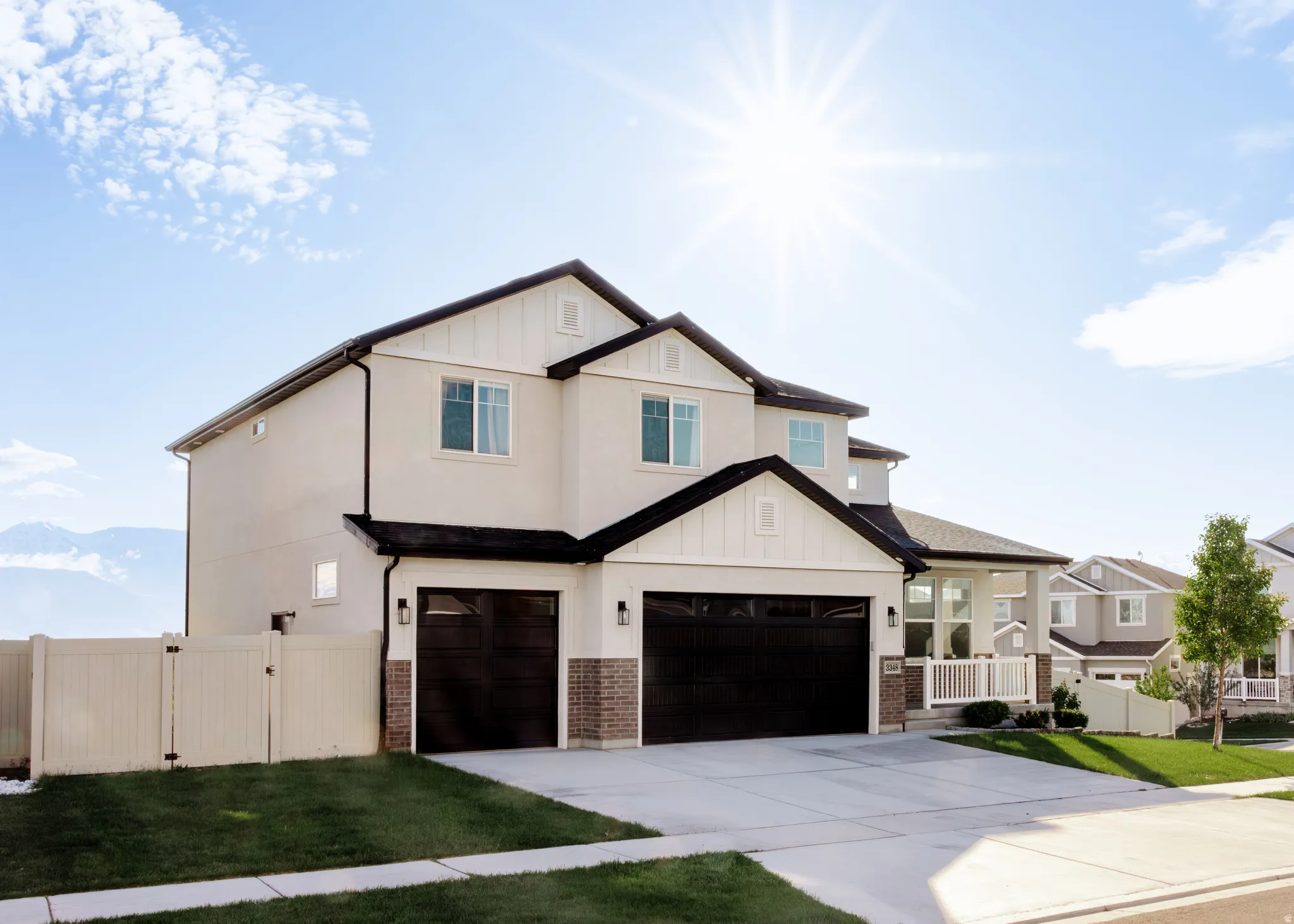Contemporary two-story residence featuring a light-toned exterior with dark trim accents, two dark garage doors, and a partial brick facade