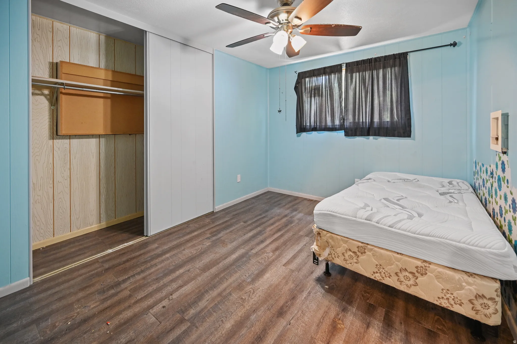 Bedroom with dark wood-style flooring, ceiling fan, a closet, and wood walls