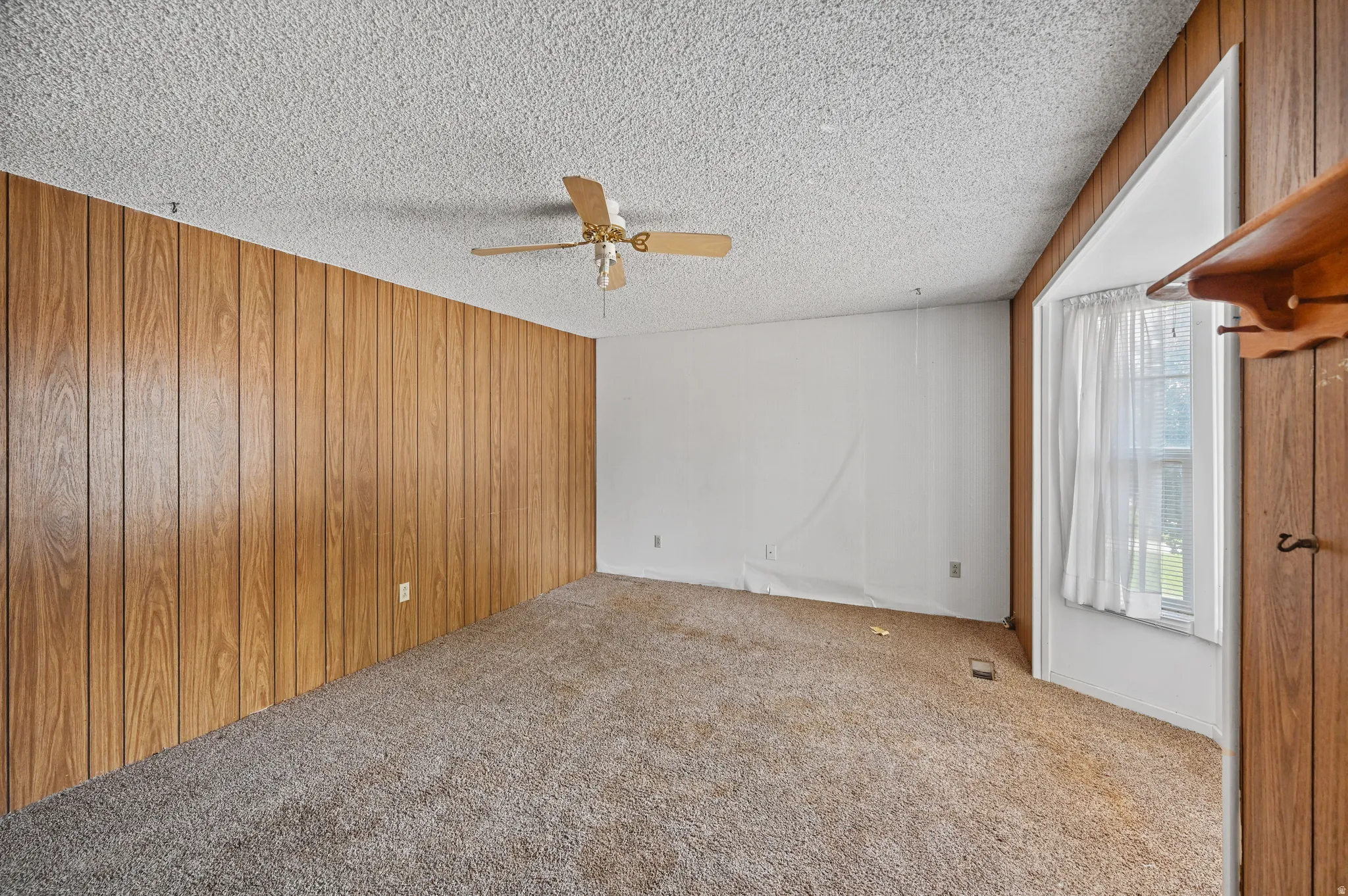 Unfurnished room with a ceiling fan, carpet, wooden walls, and a textured ceiling
