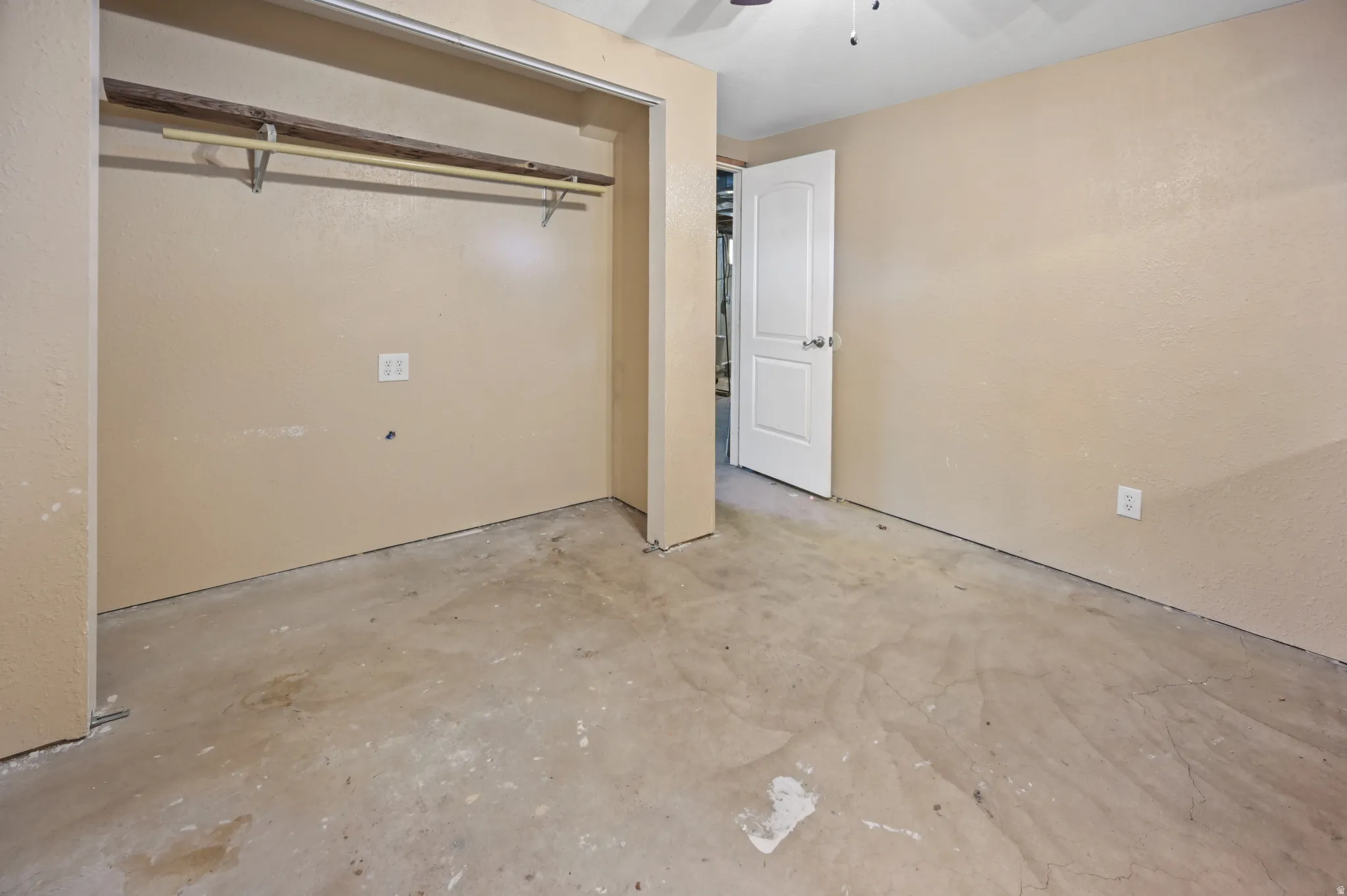 Unfurnished bedroom featuring unfinished concrete floors, a ceiling fan, a closet, and a textured wall