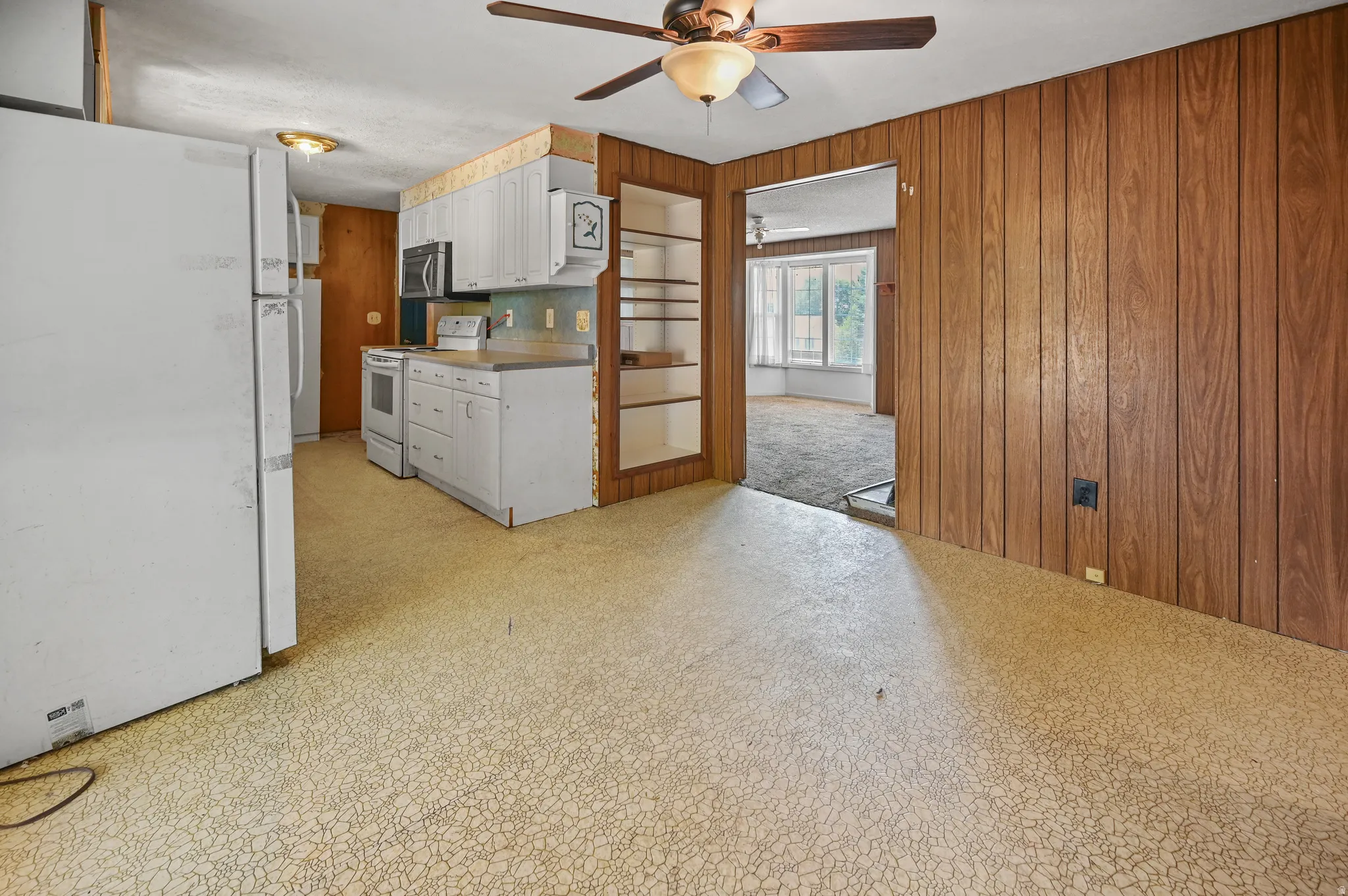 Kitchen featuring white appliances, light floors, wooden walls, white cabinets, and ceiling fan