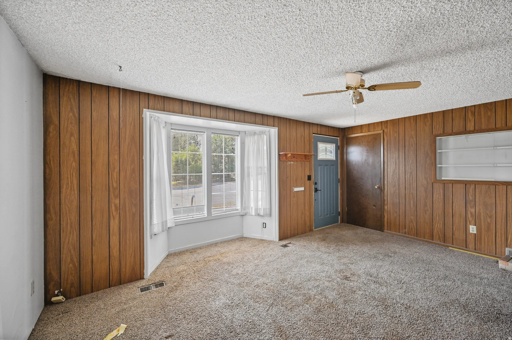 Carpeted entryway featuring a ceiling fan, a textured ceiling, and wood walls