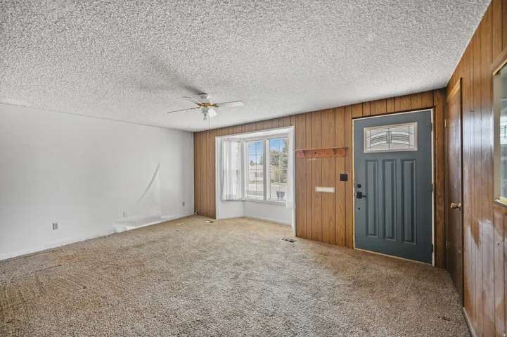 Carpeted foyer featuring a ceiling fan, wood walls, and a textured ceiling