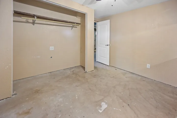 Unfurnished bedroom featuring unfinished concrete floors, a ceiling fan, a closet, and a textured wall