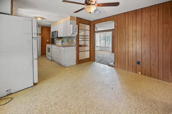 Kitchen featuring white appliances, light floors, wooden walls, white cabinets, and ceiling fan