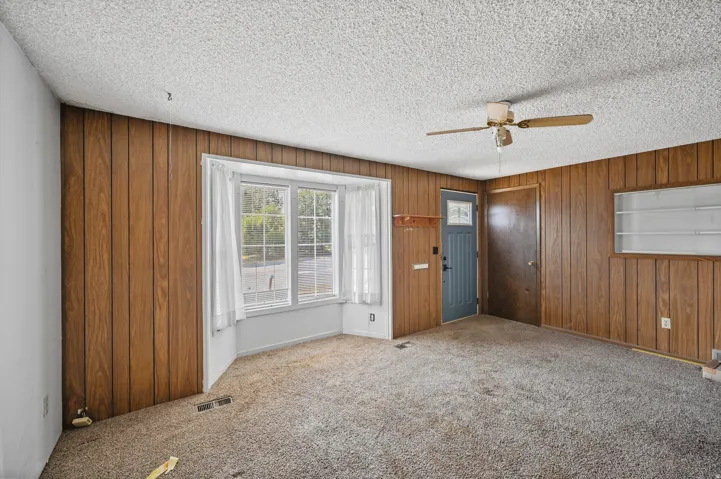Carpeted entryway featuring a ceiling fan, a textured ceiling, and wood walls
