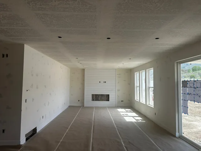 Unfurnished living room featuring a large fireplace and wallpapered walls
