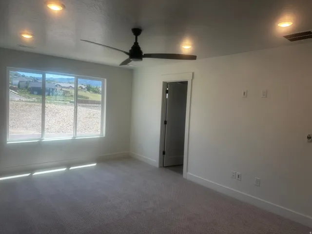 Spacious room featuring a multi-pane window, flush-mount ceiling fan, recessed lighting, and neutral carpeting