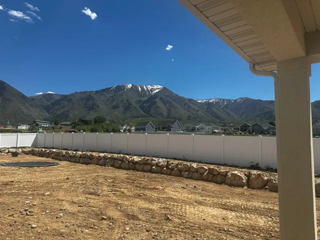 Expansive undeveloped backyard featuring a vinyl privacy fence and a natural stone retaining wall