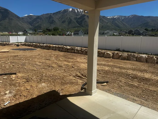 Expansive backyard featuring a concrete patio, a stone retaining wall, and a white privacy fence