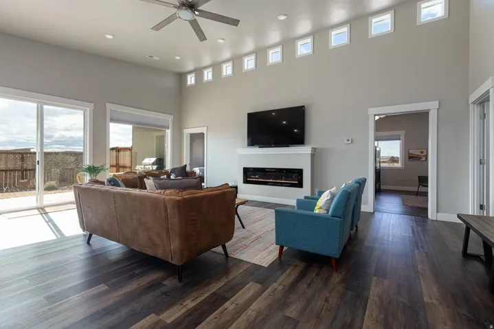Living room featuring dark wood-type flooring, a ceiling fan, a high ceiling, a glass covered fireplace, and recessed lighting