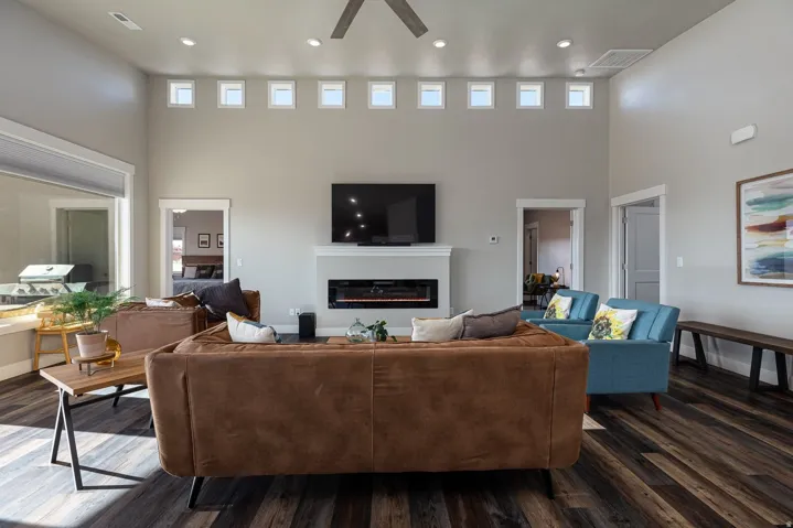 Living area with a high ceiling, ceiling fan, a glass covered fireplace, dark wood-type flooring, and recessed lighting
