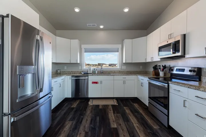 Kitchen featuring stainless steel appliances, white cabinets, dark wood-type flooring, recessed lighting, and light stone countertops