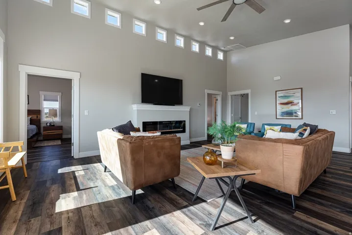 Living room with a high ceiling, dark wood-style flooring, a glass covered fireplace, ceiling fan, and recessed lighting
