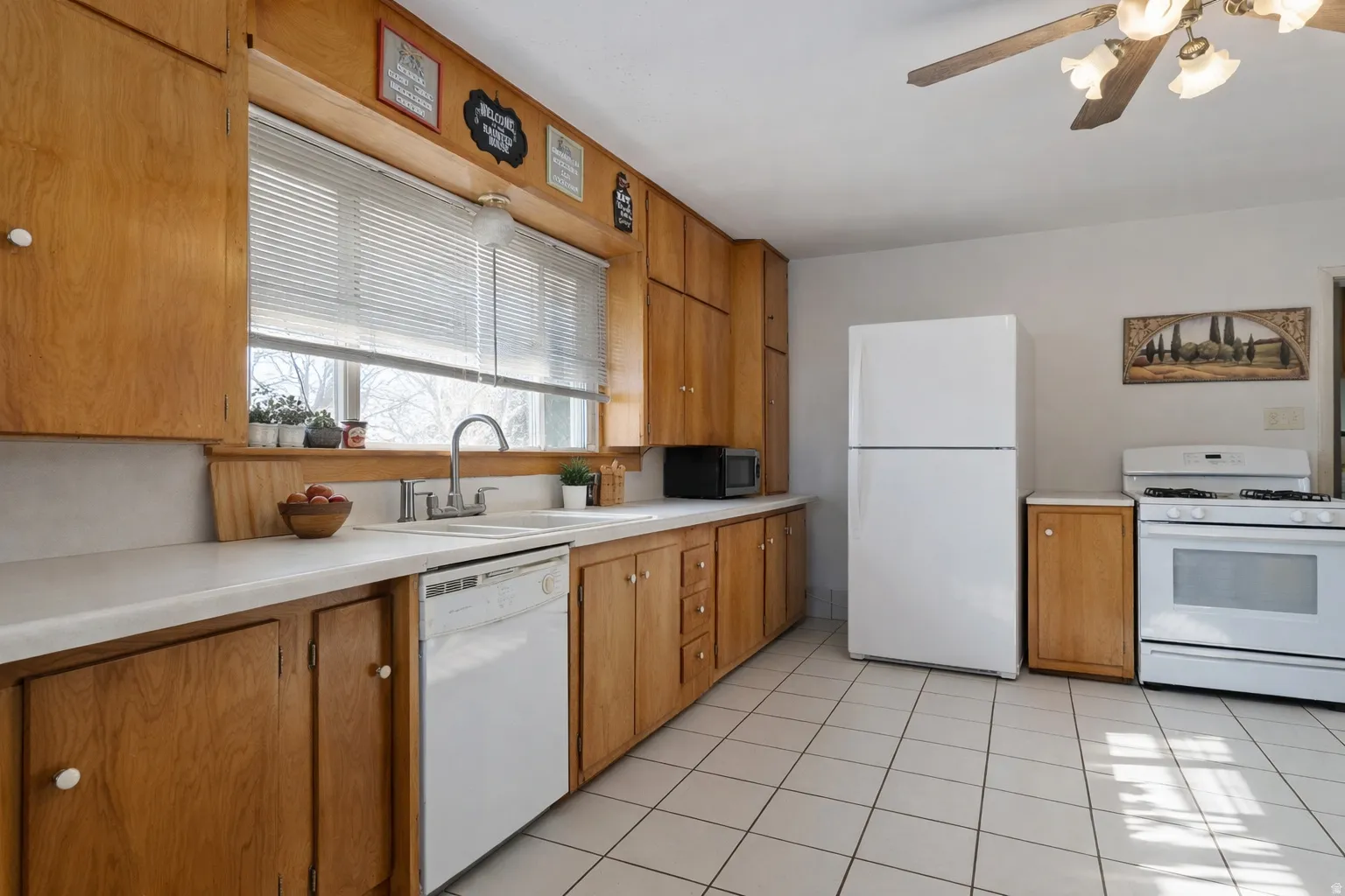 Kitchen featuring white appliances, light countertops, wood finish cabinetry, a ceiling fan, and light tile patterned flooring