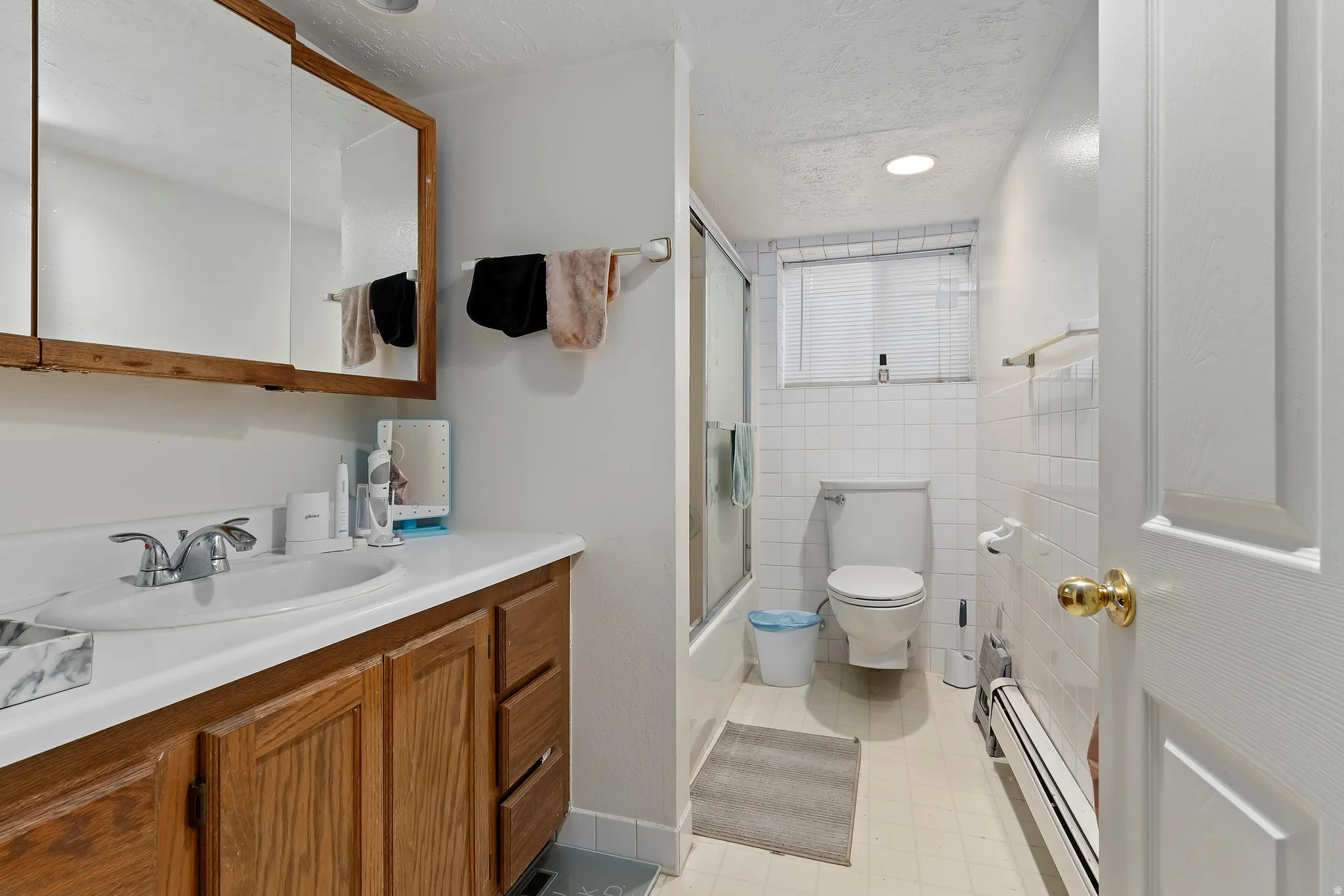 Full bathroom with a baseboard heating unit, combined bath / shower with glass door, vanity, tile walls, and a textured ceiling