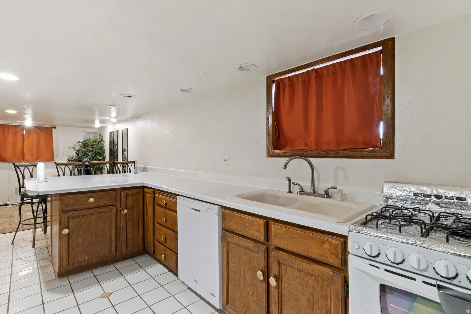 Kitchen featuring range with gas cooktop, light countertops, white dishwasher, a peninsula, and a kitchen breakfast bar