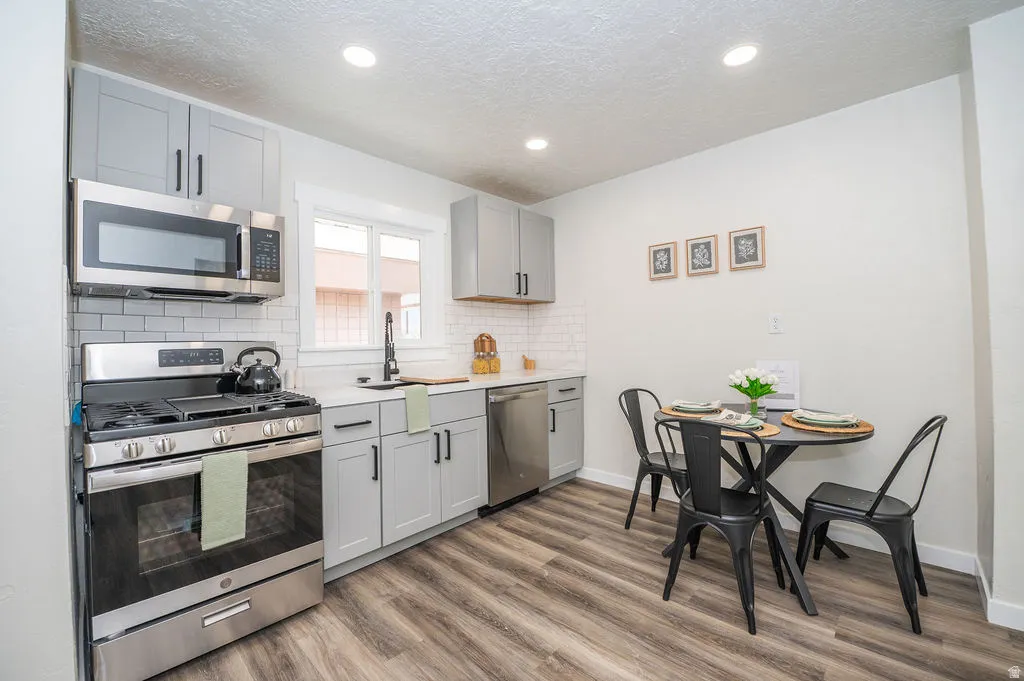 Kitchen featuring stainless steel appliances, gray cabinetry, dark wood-style flooring, backsplash, and a textured ceiling