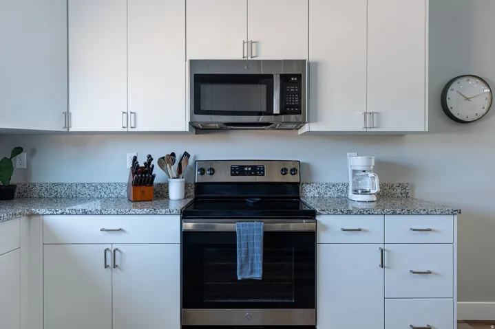 Kitchen with stainless steel appliances, white cabinets, and light stone countertops