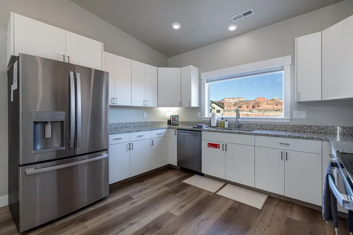 Kitchen featuring stainless steel appliances, white cabinetry, light stone counters, dark wood-style floors, and lofted ceiling