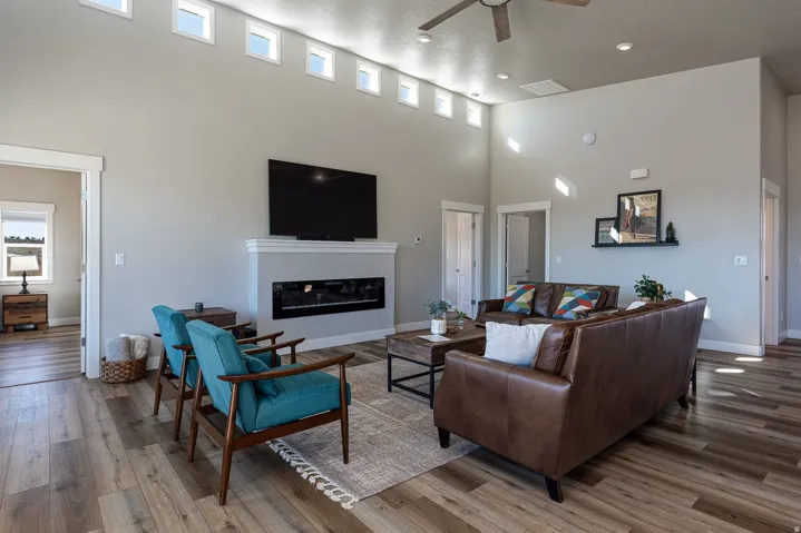 Living area with ceiling fan, a high ceiling, wood finished floors, and a glass covered fireplace