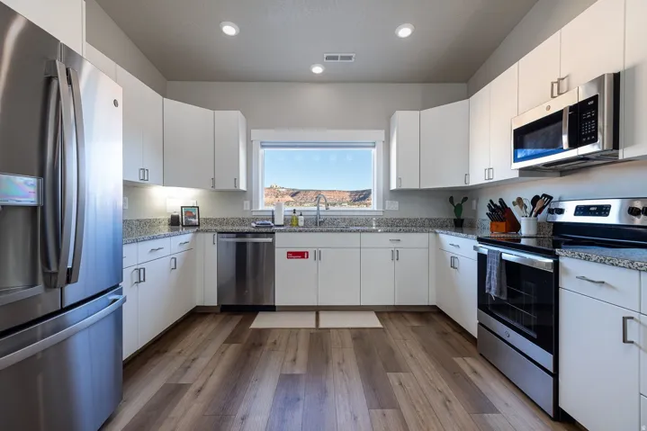 Kitchen featuring stainless steel appliances, white cabinets, light stone counters, dark wood-style floors, and recessed lighting