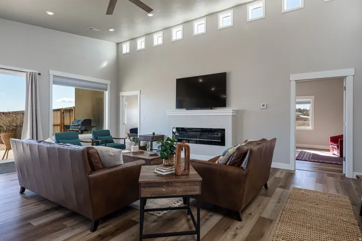 Living area with a high ceiling, a ceiling fan, a glass covered fireplace, and dark wood-type flooring