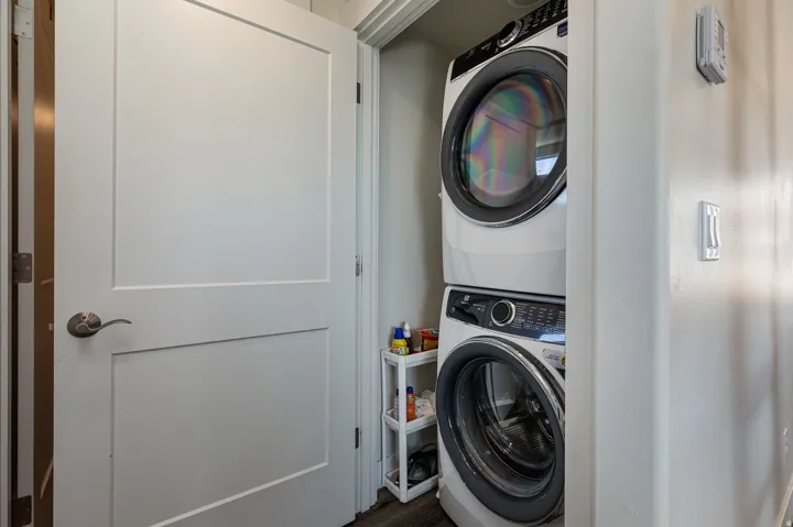 Laundry area with stacked washing machine and dryer and dark wood-type flooring