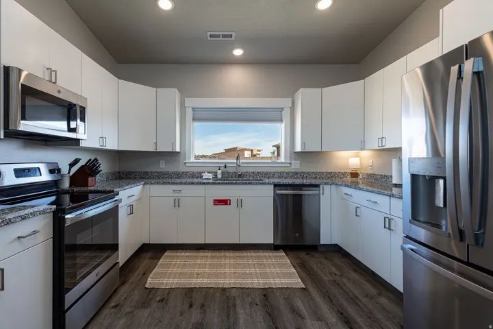 Kitchen with stainless steel appliances, white cabinets, dark stone counters, recessed lighting, and dark wood finished floors