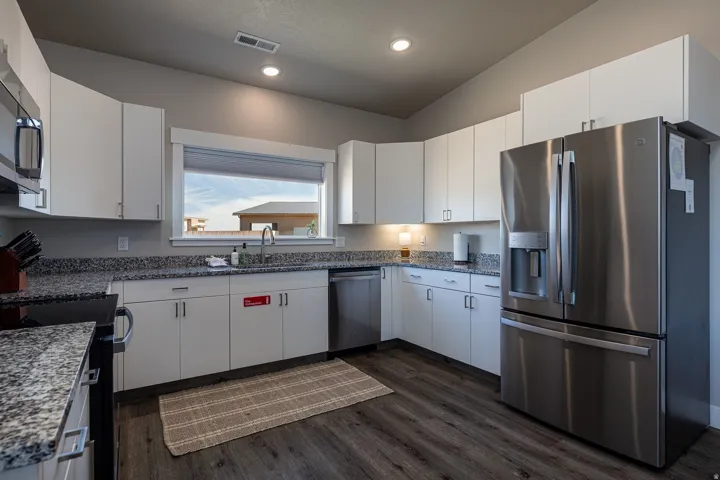 Kitchen with stainless steel appliances, dark stone counters, white cabinets, dark wood finished floors, and recessed lighting
