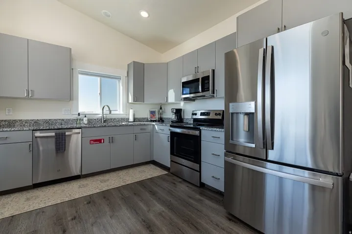 Kitchen featuring gray cabinets, stainless steel appliances, vaulted ceiling, dark wood-style floors, and dark stone counters
