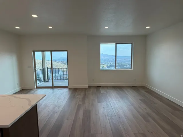 Open-concept living area featuring wood-finish flooring, recessed lighting, and a sliding glass door opening to a balcony with metal railings