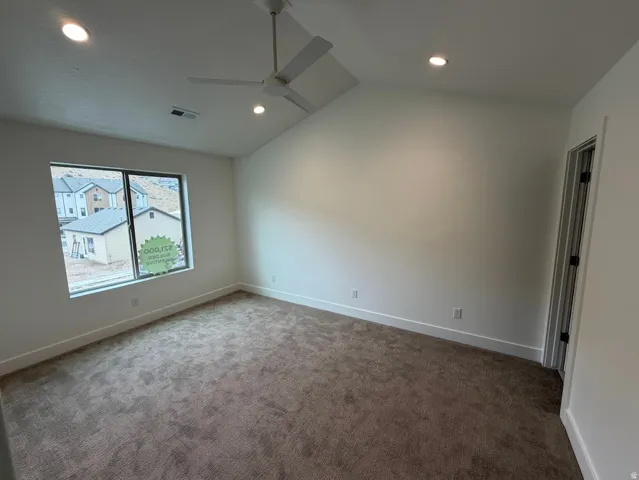 Spacious room featuring vaulted ceilings, recessed lighting, a modern ceiling fan, expansive window, and neutral-tone carpeting