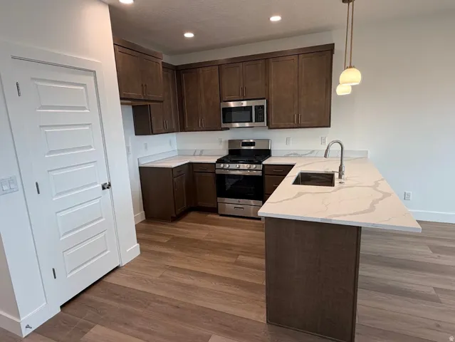 Kitchen featuring wood-finish flooring, dark wood cabinetry, stainless steel appliances, and light-toned countertops with an integrated sink and gooseneck faucet