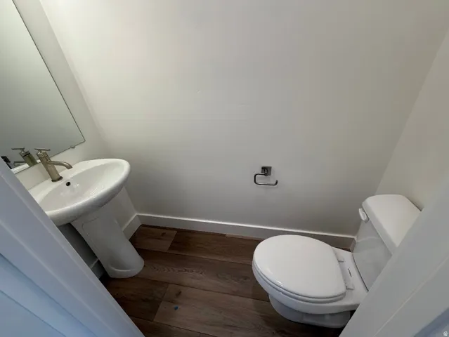 Powder room featuring a pedestal sink with a brushed brass faucet, dark wood-finish flooring, white baseboards, and a white toilet
