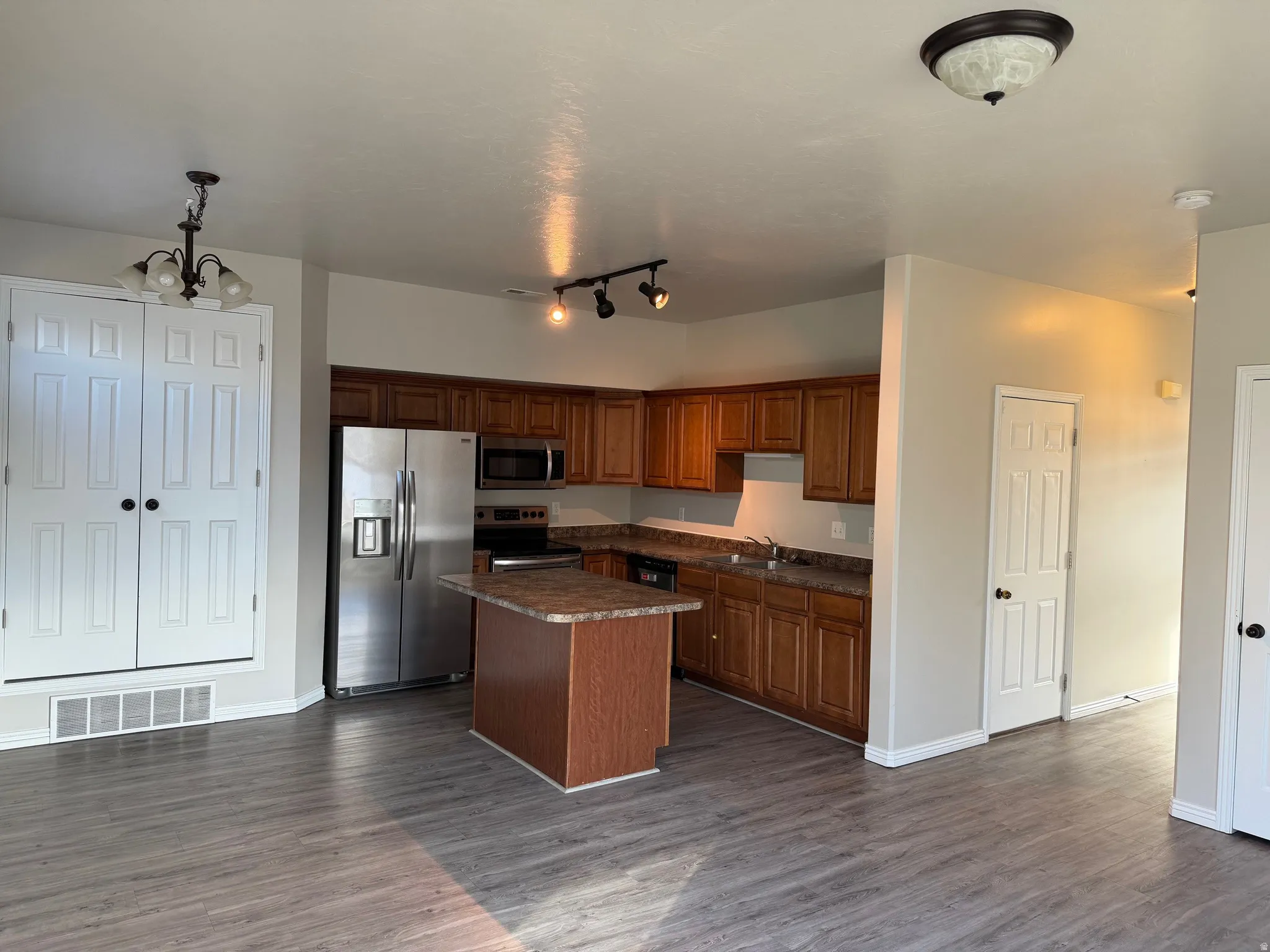 Kitchen featuring stainless steel appliances, wood finish cabinetry, dark wood-type flooring, and a center island