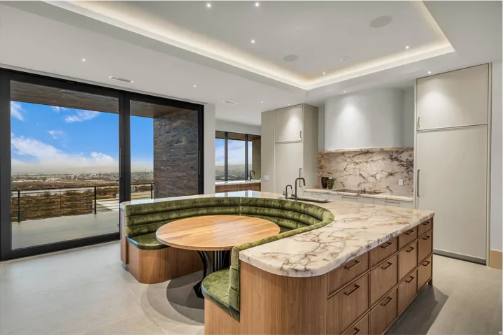 Kitchen with modern cabinets, expansive windows, a kitchen island with sink, light stone countertops, and tasteful backsplash