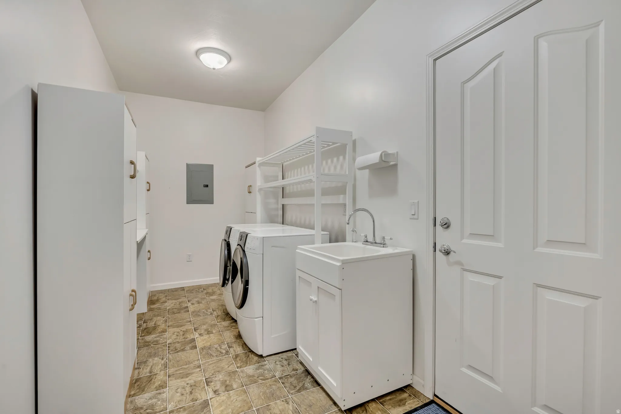 Laundry room with washing machine and dryer, stone finish flooring, electric panel, and cabinet space