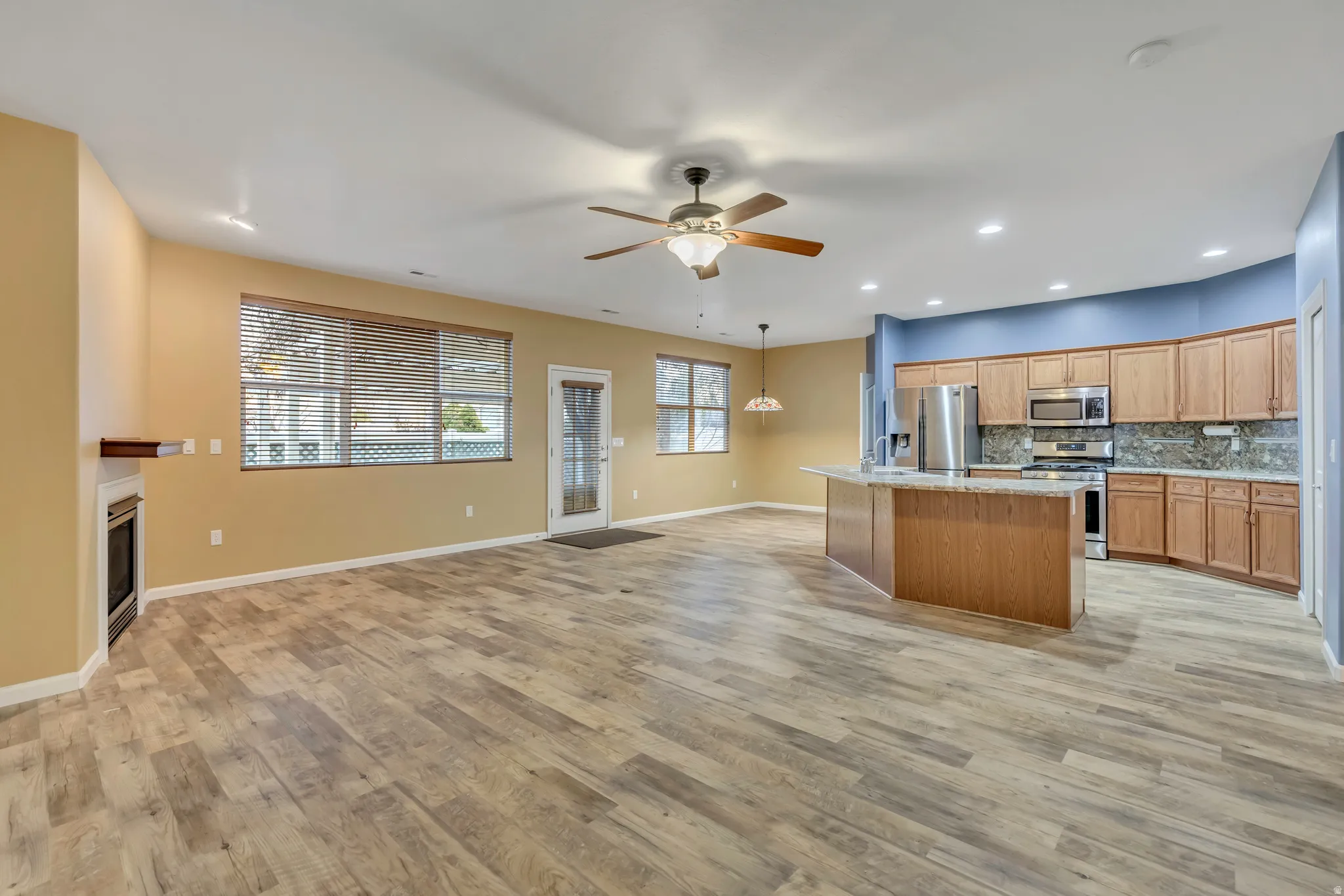 Kitchen featuring open floor plan, stainless steel appliances, a ceiling fan, backsplash, and a kitchen island