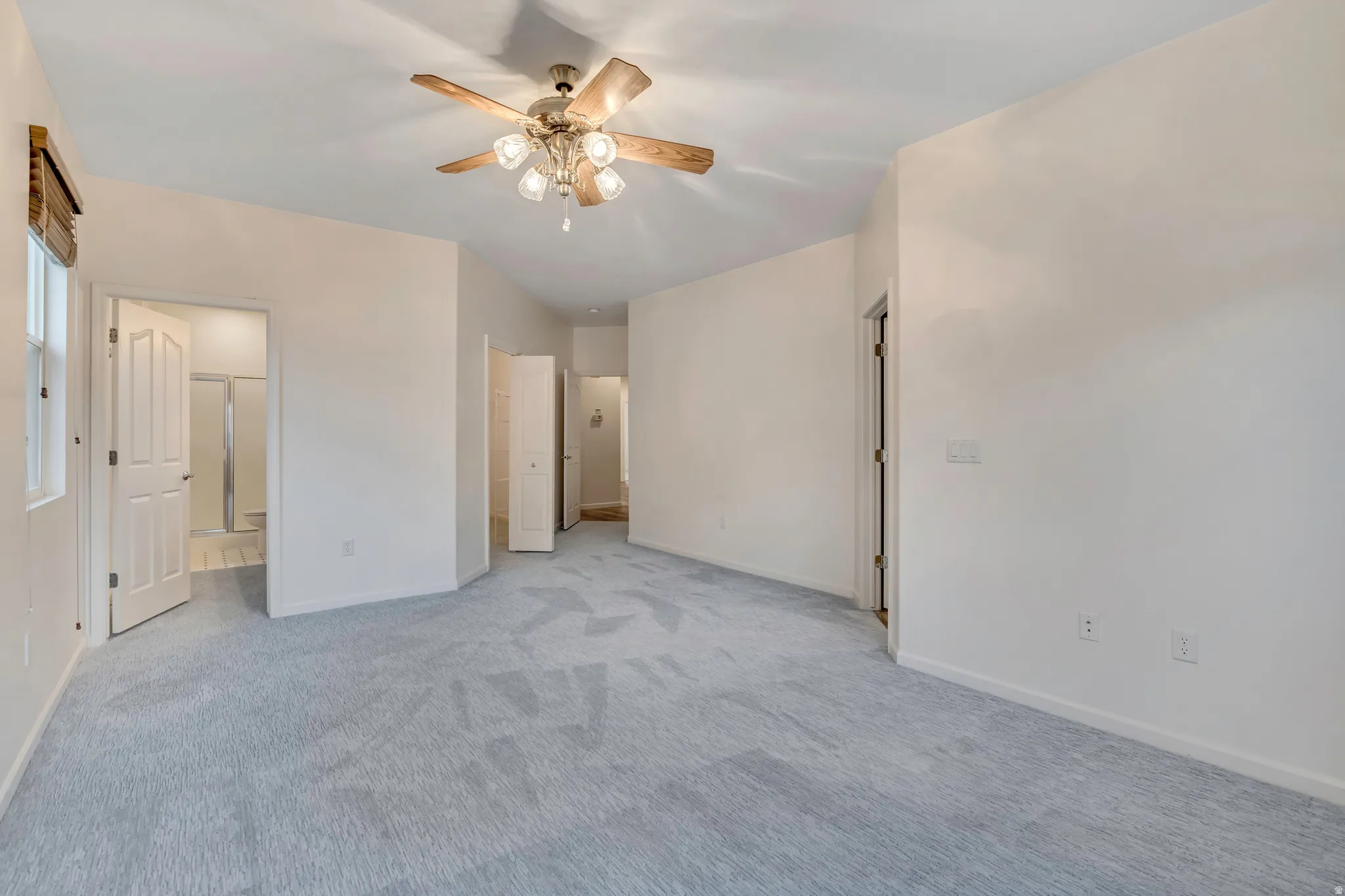 Unfurnished bedroom with connected bathroom, light carpet, and a ceiling fan
